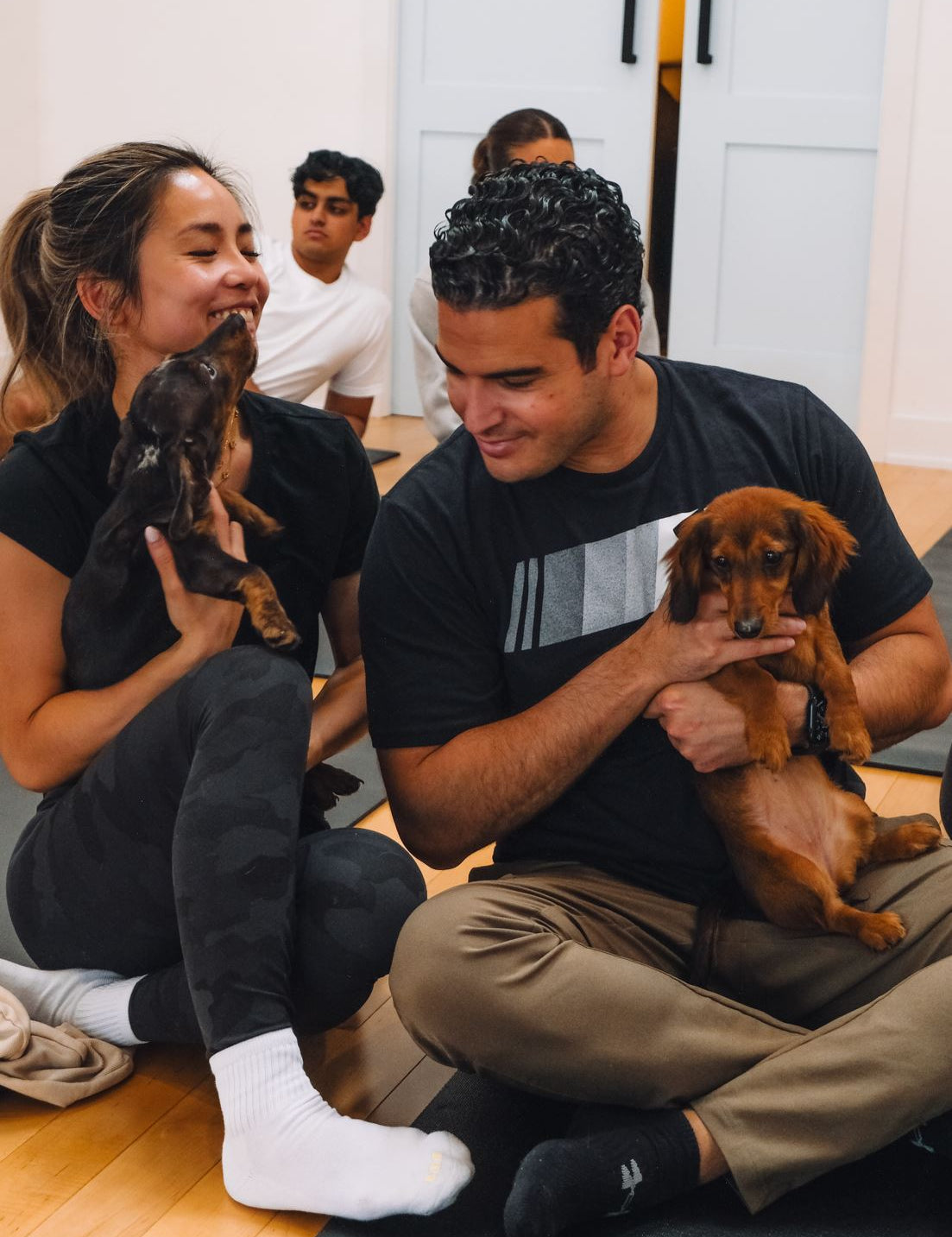 Two guests cuddling mini dachshund puppies during a puppy yoga class at Therapy Puppy Studio
