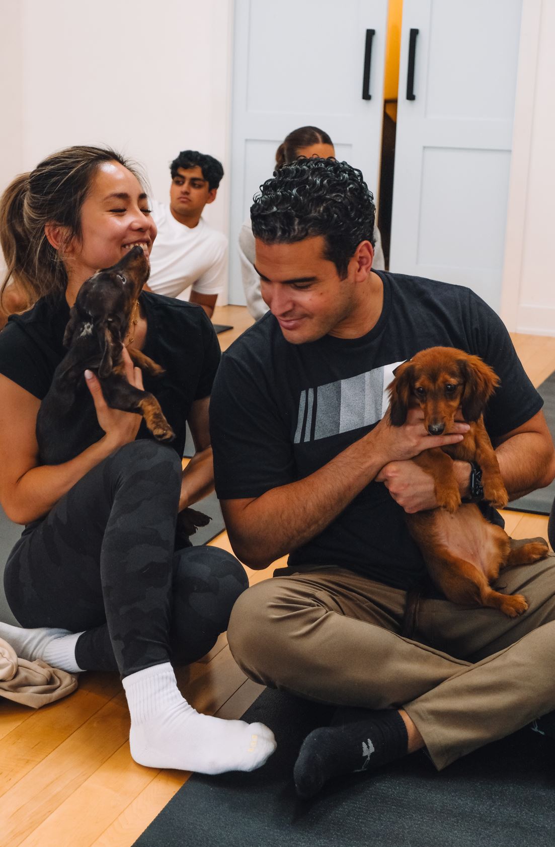Two guests cuddling mini dachshund puppies during a puppy yoga class at Therapy Puppy Studio